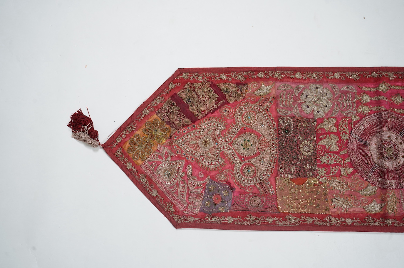 An Indian 20th century red silk marriage banner/hanging, ornately embroidered in silver and gold thread, with raised stump work flowers, corded and designed using simulated pearls and coloured beads etc., 74cm x 43cm. Co